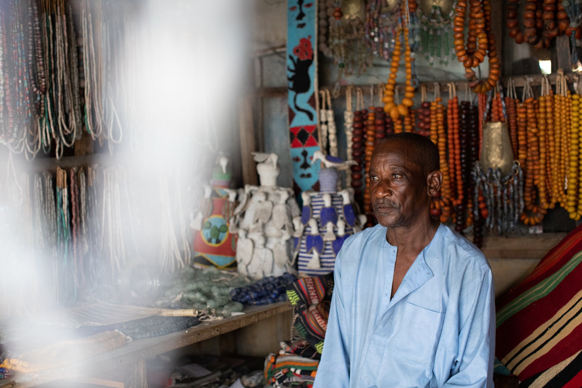 Shop owner surrounded by colorful artwork and accessories at a market